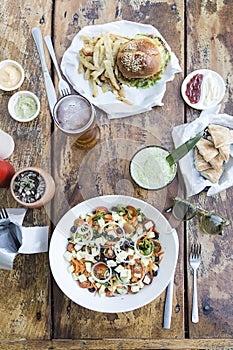 Burger with french fries and cheese salad, lettuce, tomato, olives, onion and cheese, with beer and fruit juice, on a wooden table