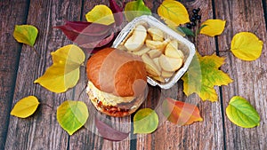 Burger and french fries on wooden background with autumn leaves,fast food concept, take away food concept, season sales