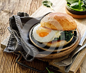 Burger with fried egg and spinach served on a plate on a wooden table