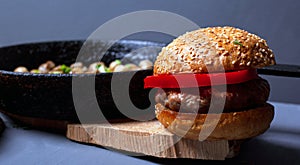 Burger with a juicy cutlet tender bun and champignon mushrooms in a castiron pan on a wooden rustic plate on a gray background.