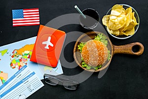 Burger, map, tickets, passport and usa flag for gastronomical tourism to America on black background top view