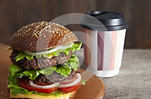 Burger with paper coffee cup to go on wooden tabletop. Close up