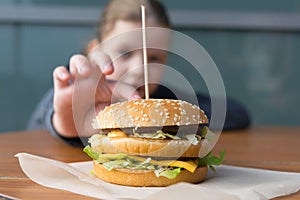 Burger on the table, in the background a girl reaches out to take a sandwich