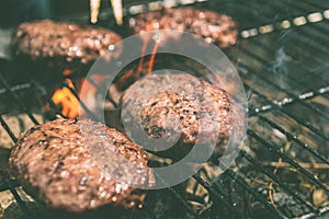 Burgers are cooking on grill with open flames