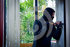 Burglar with crowbar trying break the window to enter the house
