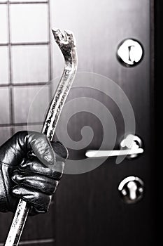 Burglar hand holding crowbar break opening door