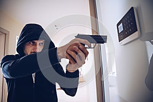 Burglar in hood holding a gun in hand breaking into the house.