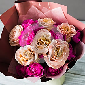 Burgundy bouquet with white and pink roses stands in a white stand on a wooden table