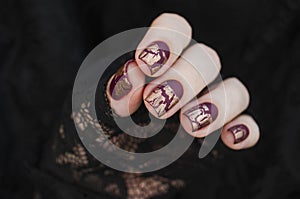 Burgundy golg cracle matte nail polish. Manicured nail with dark matte nail polish isolated on black