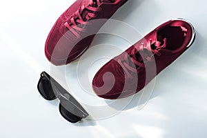 Burgundy sneakers on a white background with nature light shadows