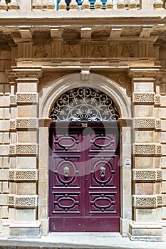 Burgundy wooden arched door decorated with gilded door knockers with lion heads