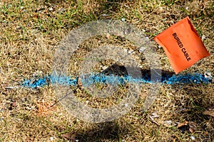 BURIED CABLE flag sign on steel rod and colored cable location marking on green grass clearly designates underground utility lines