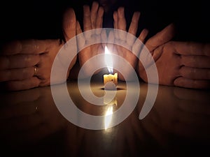 Buring candle, Four hands in background. Dark room