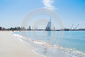 Burj Al Arab in Jumeirah Island or boat building with waves on sea beach, Dubai Downtown skyline, United Arab Emirates or UAE.