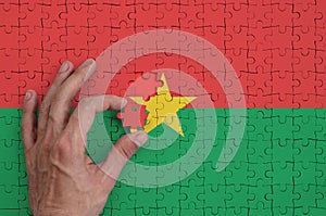 Burkina Faso flag is depicted on a puzzle, which the man`s hand completes to fold