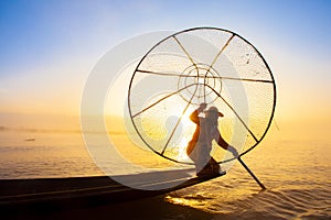 Burmese fisherman on bamboo boat catching fish in traditional way with handmade net. Inle lake, Myanmar Burma travel destination