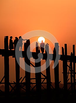 People crossing the longest teak bridge in the world, the iconic wooden U Bein Bridge during sunset, Mandalay, Myanmar