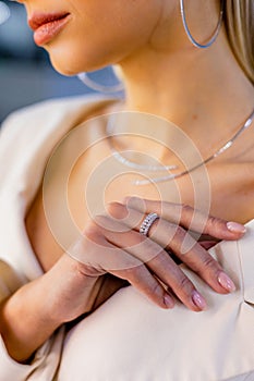 Burn an elegant diamond ring on the female finger, necklace and large round earrings. Girl stands in a jewerly store