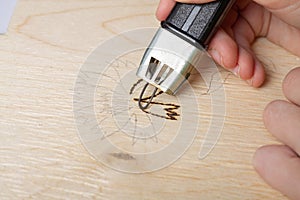 Burn out a drawing on a wooden board with an electric device with a scorcher