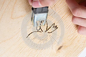 Burn out a drawing on a wooden board with an electric device with a scorcher