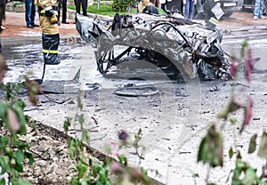 Burned car after an accident on the road. Firefighters standing nearby. Reportage picture in street.