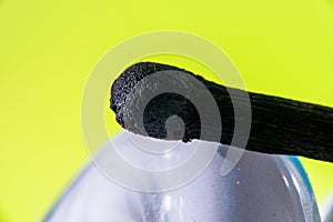 Burned match on the surface of a curly light bulb. On a light green background. Macro