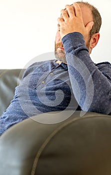 Burned out man in his forties sitting on the couch with his head in his hand