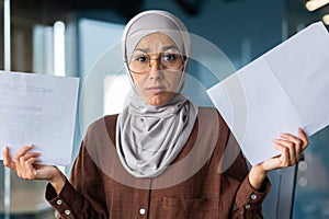 Burned out at work, financial problems. Portrait of a young hijabi Muslim woman sitting in the office, looking worriedly