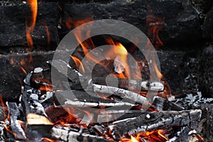 Burned Wood with flames still burning, dark Stone Background of camp fire or Grill