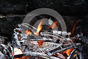 Burned Wood with flames still burning, dark Stone Background of camp fire or Grill