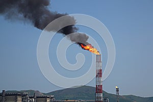 Burning accompanying gas from refinery stack against blue sky photo