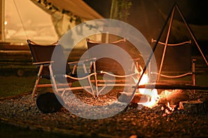 Burning bonfire and folding chairs near camping tent.