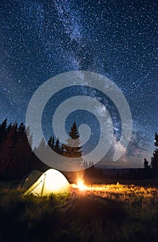 Burning bonfire and tents under bright starry sky on which the Milky Way is clearly visible. Magical sky
