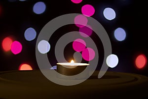Burning candle on a background with colorful lights. Holiday accessories at dusk