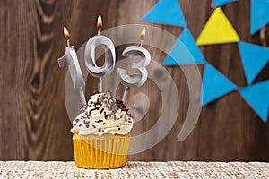 Burning candle - birthday number 103 on wooden background with pennants