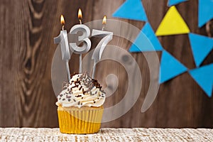 Burning candle - birthday number 137 on wooden background with pennants