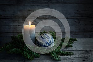 Burning candle and a blue Christmas ball on fir tree branches against a dark gray background from rustic wooden planks, copy space