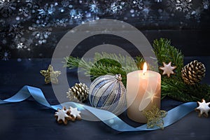 Burning candle and blue Christmas bauble, surrounded by fir branches, cinnamon stars and a ribbon against a night blue wooden