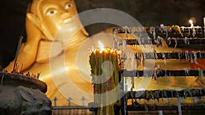 Burning candle at a buddhist cave temple with lying golden buddha on background. hd slowmotion. thailand.