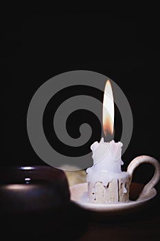 A burning candle on a candlestick, holy bible and meditation on a dark background