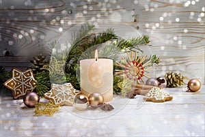 Burning candle with Christmas decoration, fir branches, baubles, straw stars and gingerbread on rustic wood, snowy boheh lights,