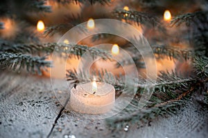 Burning candle and Christmas decoration over snow with pine branches on white wooden background