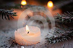 Burning candle and Christmas decoration over snow with pine branches on white wooden background