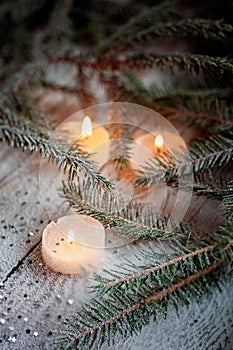Burning candle and Christmas decoration over snow with pine branches on white wooden background