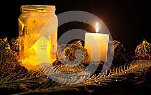 Burning candle and an empty jar with yellow reflection with Christmas decorations