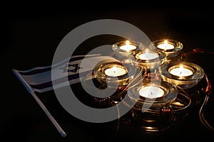 Burning candle and flag of Israel on black background. Holocaust memory day