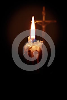A burning candle in the foreground and a cross