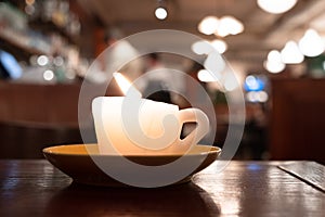 Burning candle in form of coffee cup on the table