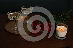 Burning candle, glasses of wine and beautiful red roses on wooden table indoors