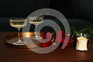 Burning candle, glasses of wine and beautiful red roses on wooden table indoors